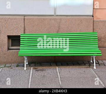Hellgrüne Bank auf Granitpflaster in der Nähe des Granitfundaments eines Hauses in Helsinki, Finnland Stockfoto
