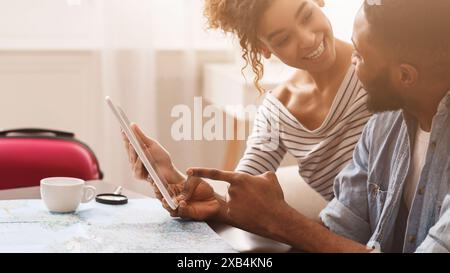 Schwarzer Mann und Frau sitzen am Tisch und schauen sich Tablet an Stockfoto