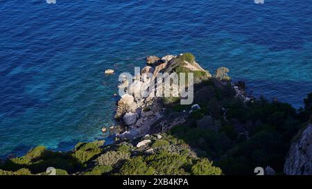 Blick von oben auf die felsige Küste, wo das blaue Meer auf die Klippen trifft, umgeben von grüner Vegetation, Kritinia Castle, St. John's Castle Stockfoto