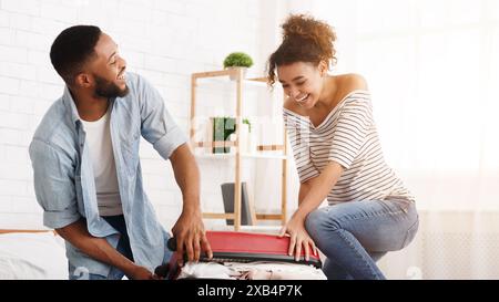 Afrikanisch-amerikanisches Paar versuchen, Koffer auf das Bett zu schließen. Stockfoto