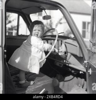 1950er Jahre, historisches Mädchen, das im Auto der Ära steht, Hände auf dem Lenkrad Stockfoto