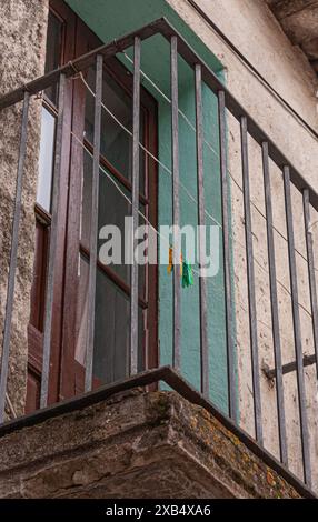 Von unten aus blickt man auf einen antiken, schwarzen Eisenbalkon mit einer Tür aus Holz und Glas. Stockfoto