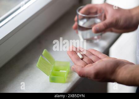 Nahaufnahme der männlichen Hände, die Kapselpille und ein Glas Wasser halten. Medizin Pharmazie Gesundheit. Nahaufnahme eines Mannes, der Pillen nimmt Stockfoto