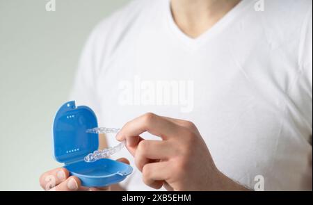 Nahaufnahme eines jungen Mannes mit unsichtbarem Zahnhalteapparat und einem Koffer zu ihrer Aufbewahrung und zum Schutz. Männliche Hände, die Zahnaligner halten Stockfoto