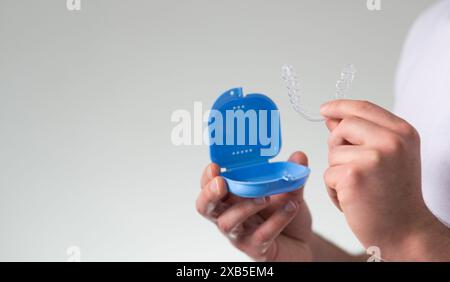 Nahaufnahme eines jungen Mannes mit unsichtbarem Zahnhalteapparat und einem Koffer zu ihrer Aufbewahrung und zum Schutz. Männliche Hände, die Zahnaligner halten Stockfoto