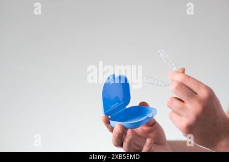 Nahaufnahme eines jungen Mannes mit unsichtbarem Zahnhalteapparat und einem Koffer zu ihrer Aufbewahrung und zum Schutz. Männliche Hände, die Zahnaligner halten Stockfoto