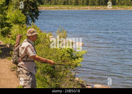 Ein älterer 70-jähriger Mann, der einen Rucksack mit Stuhl trägt, fischt an einem See, nachdem er hineingewandert ist. Stockfoto