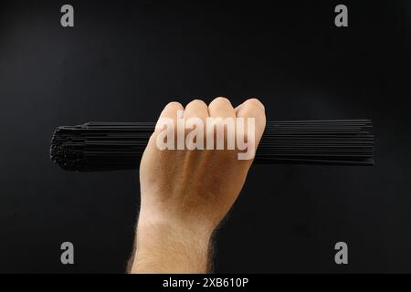 Nahaufnahme eines jungen kaukasischen Mannes mit einem Haufen ungekochter schwarzer Spaghetti in der Hand vor schwarzem Hintergrund Stockfoto