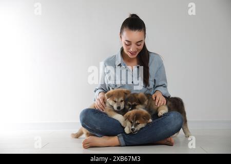 Frau mit Akita Inu Welpen, die auf dem Boden neben einer hellen Wand sitzen Stockfoto