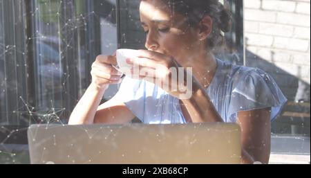 Junge kaukasische Frau trinkt Kaffee, während sie am Laptop arbeitet Stockfoto