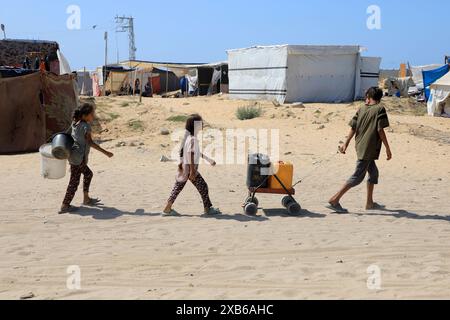 Gaza. Juni 2024. Vertriebene Kinder holen am 10. Juni 2024 Wasser im Gebiet von al-Mawasi im südlichen Gazastreifen in Khan Younis. Am 7. Mai weitete das israelische Militär seine Operationen in Rafah aus und leitete über 1,5 Millionen Palästinenser an, nach Khan Younis und anderen zentralen Gaza-Gebieten zu ziehen. Das Hilfswerk der Vereinten Nationen für Palästinaflüchtlinge im Nahen Osten (UNRWA) schätzt, dass in diesen Gebieten derzeit etwa 1,7 Millionen Menschen untergebracht sind. Quelle: Rizek Abdeljawad/Xinhua/Alamy Live News Stockfoto