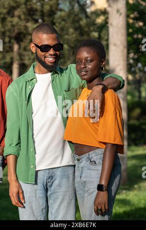 Glücklicher afroamerikaner, der lächelnd eine Freundin umarmt, die draußen steht und in die Kamera schaut. Stockfoto