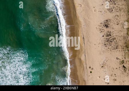 Blick aus der Vogelperspektive auf die Meereswellen, die einen abgelegenen Sandstrand waschen Stockfoto