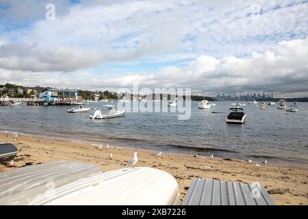 Watsons Bay Beach mit Ruderbootladen am Ufer und Blick über den Hafen zum Stadtzentrum von Sydney und CBD mit Hochhäusern, NSW, Australien Stockfoto