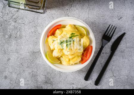 Kartoffelsalat mit Tomaten und Zitrone auf grauem Steintisch Stockfoto