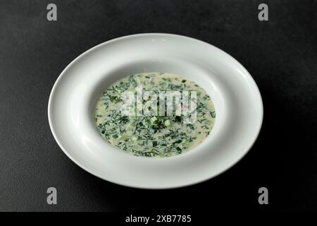 Kalte Suppe mit frischen Gurken, Wurst, Brühe und Sauerrahm in einem Tellerhut auf schwarzem Hintergrund. Ein traditionelles Gericht ist Okroshka. Stockfoto