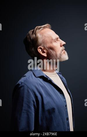 Vertikales Seitenporträt eines bärtigen älteren Mannes mit lässiger Kleidung, der im Studio nach oben blickt Stockfoto