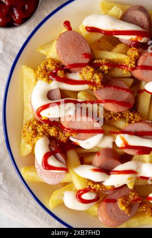 Hausgemachte Salchipapa-Pommes mit Ketchup, Senf und Mayo auf einem Teller, Blick von oben. Nahaufnahme. Stockfoto