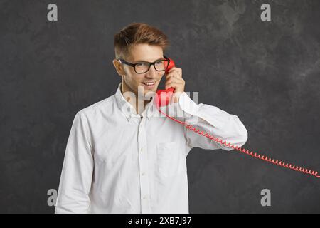 Glücklicher, lächelnder junger Mann, der mit dem Kundensupport über ein Retro-Festnetztelefon spricht Stockfoto