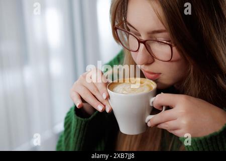 Eine Frau, die eine Brille trägt, sieht glücklich aus, als sie eine köstliche Tasse Kaffee isst Stockfoto