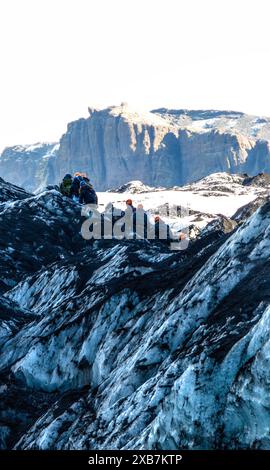 Eine Gruppe von Menschen läuft über den Solheimajokull-Gletscher in Island. Die Leute tragen orangefarbene Helme. Die Szene ist abenteuerlich und aufregend Stockfoto