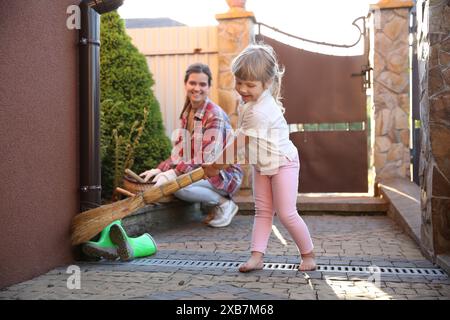 Mutter und ihre süße Tochter putzen zusammen in der Nähe des Hauses am Frühlingstag Stockfoto