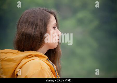 Eine Frau mit langen braunen Haaren trägt eine gelbe Jacke. Sie blickt in die Ferne Stockfoto