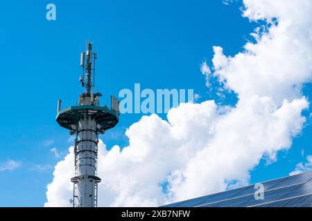 Sendemast und Teil des Daches mit Solarpaneelen vor blauem Himmel mit weißen Wolken. Stockfoto