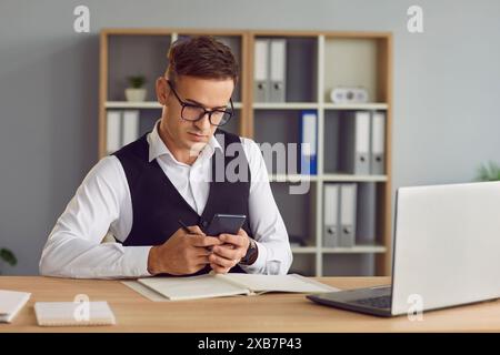 Seriöser Geschäftsmann, Der Im Büro Mit Dem Smartphone Am Schreibtisch Arbeitet Stockfoto
