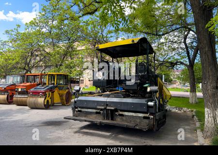 Abgenutzte Baumaschinen zum Verlegen von Asphalt stehen am Straßenrand. Stockfoto