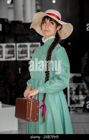 Eine weibliche Cosplayer in einem türkisfarbenen Kleid und einem breitkrempigen Strohhut. Stockfoto