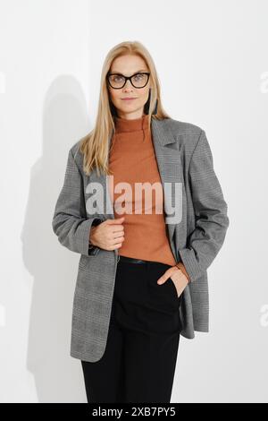 Porträt einer stilvoll gekleideten Frau, die eine Hand in der Hosentasche und die andere am Saum ihres karierten Blazers hält Stockfoto