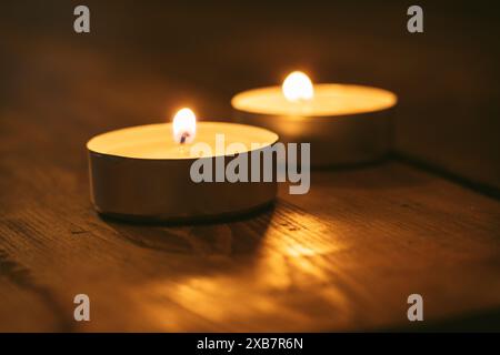 Teelichterkerzen mit Flamme auf Holztisch im dunklen Raum Stockfoto