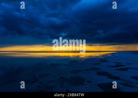 Atemberaubender Sonnenuntergang mit leuchtenden Farben über einem ruhigen Meer unter dunklen Sturmwolken, die eine dramatische und friedliche Szene schaffen. Stockfoto