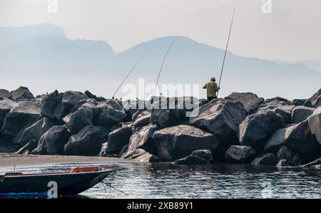 Zwei Individuen fischen auf Felsen neben einem Gewässer Stockfoto