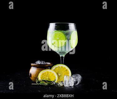 Grüner Zitronenwein im Glas mit Eiswürfeln und Limette auf schwarzem Hintergrund Stockfoto