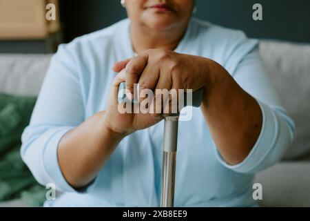 Nicht erkennbarer reifer afroamerikanischer Patient, der beim Sitzen auf dem Sofa einen Gehstock greift Stockfoto