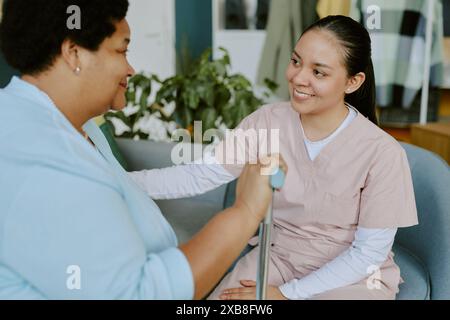 Junge und lächelnde Krankenschwester, die reife afroamerikanische Patientin beruhigt, während sie auf dem Sofa sitzt Stockfoto