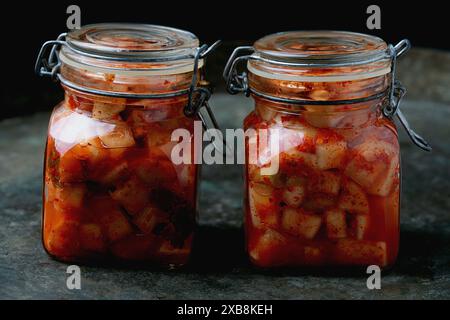 Glasgefäß gefüllt mit traditionellem koreanischem Rettich Kimchi Kkakdugi, einem scharfen und fermentierten Rettich, auf einem rustikalen dunklen Hintergrund. Stockfoto