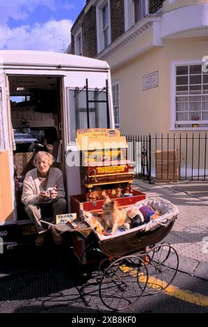 Eine Frau mit ihren Hunden in Springpferden in einem Kinderwagen. Sie ist eine Buskerin. Sie sitzt vor ihrem Wagen, wo sie wohnt und trinkt eine Tasse Tee. Auf der Tafel steht: "Ein Hund ist fürs Leben nicht nur Weihnachten. Portobello Road Samstag Floh und Antiquitätenmarkt London 1990er Jahre 1999 UK HOMER SYKES Stockfoto