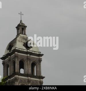 Ein Kirchturm mit rostweißer Fassade und einem Metallkreuz oben Stockfoto