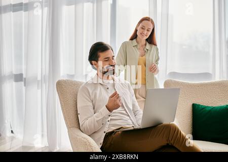 Eine rothaarige Frau und ein bärtiger Mann sitzen auf einer Couch und benutzen zusammen einen Laptop in einer modernen Wohnung. Stockfoto