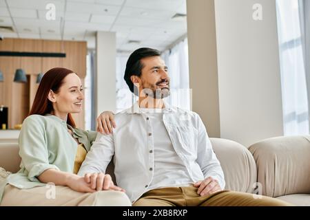 Ein wunderschönes erwachsenes Paar, eine rothaarige Frau und ein bärtiger Mann, genießen einen gemütlichen Moment zusammen auf einer modernen Wohnzimmercouch. Stockfoto