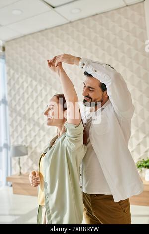 Ein bärtiger Mann und eine rothaarige Frau tanzen fröhlich in einem Büro und bringen Leben und Energie in den Arbeitsbereich. Stockfoto