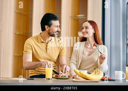 Ein bärtiger Mann und eine rothaarige Frau genießen ein gemütliches Frühstück in einer modernen Küche, was eine warme und harmonische Szene schafft. Stockfoto