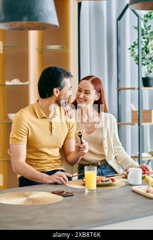 Eine rothaarige Frau und ein bärtiger Mann sitzen an einem Tisch in einer modernen Küche und teilen einen ruhigen Moment zusammen. Stockfoto