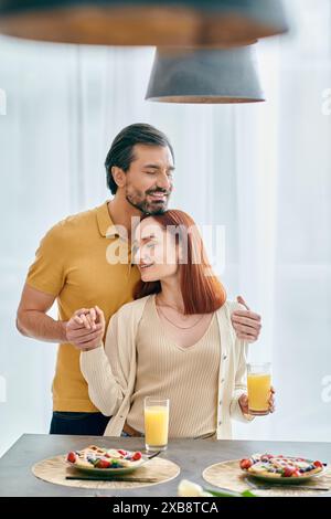 Junge rothaarige Frau und bärtiger Mann, der liebevoll am Küchentisch in einer modernen Wohnung steht. Stockfoto