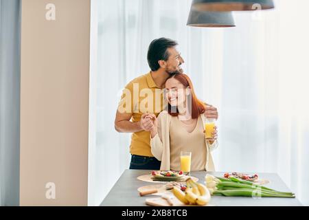 Eine rothaarige Frau und ein bärtiger Mann genießen das gemeinsame Frühstück in einer modernen Küche und teilen einen Moment der Verbundenheit und Liebe. Stockfoto