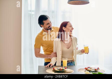 Eine rothaarige Frau und ein bärtiger Mann genießen das gemeinsame Frühstück in einer modernen Wohnung und verbinden sich über Essen und Unterhaltung. Stockfoto