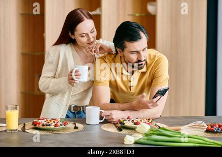 Eine rothaarige Frau und ein bärtiger Mann, die in ihre Telefone verwickelt waren, während sie in einer modernen Wohnung frühstückten. Stockfoto